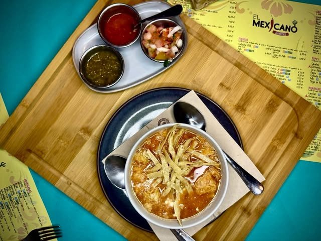 Sopa azteca con tiras de tortilla frita, acompañada de pico de gallo y salsas verde y roja